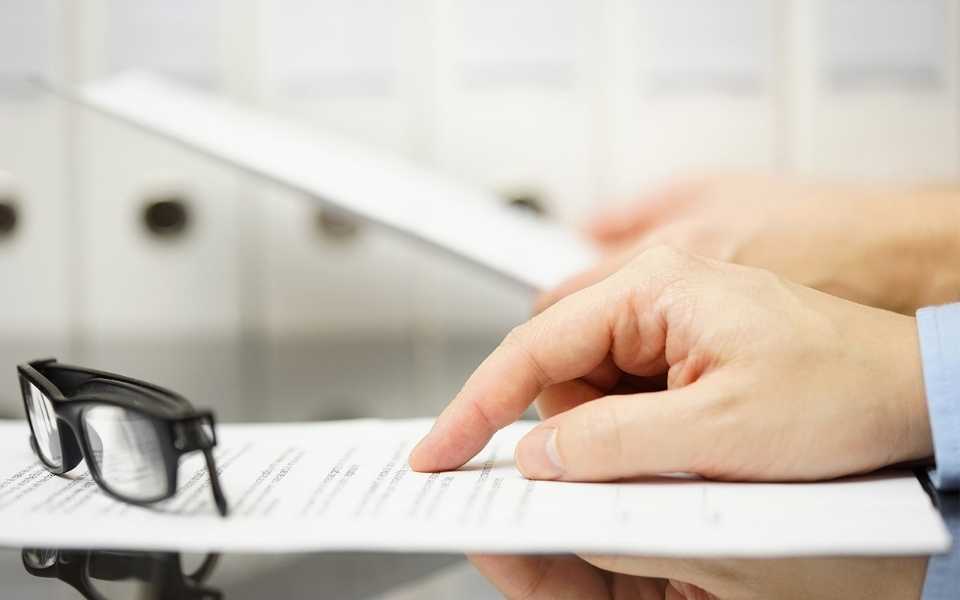 A hand pointing the finder to a paper with glasses on table.