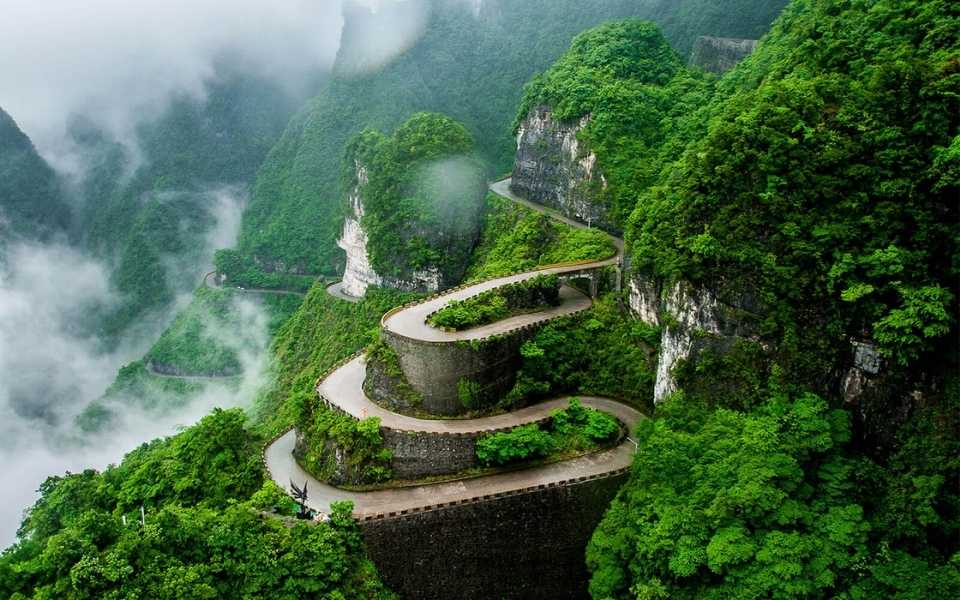Winding road between mountains and trees in mist clouds, Hunan Province, China. Concept of Chinese translation services. 