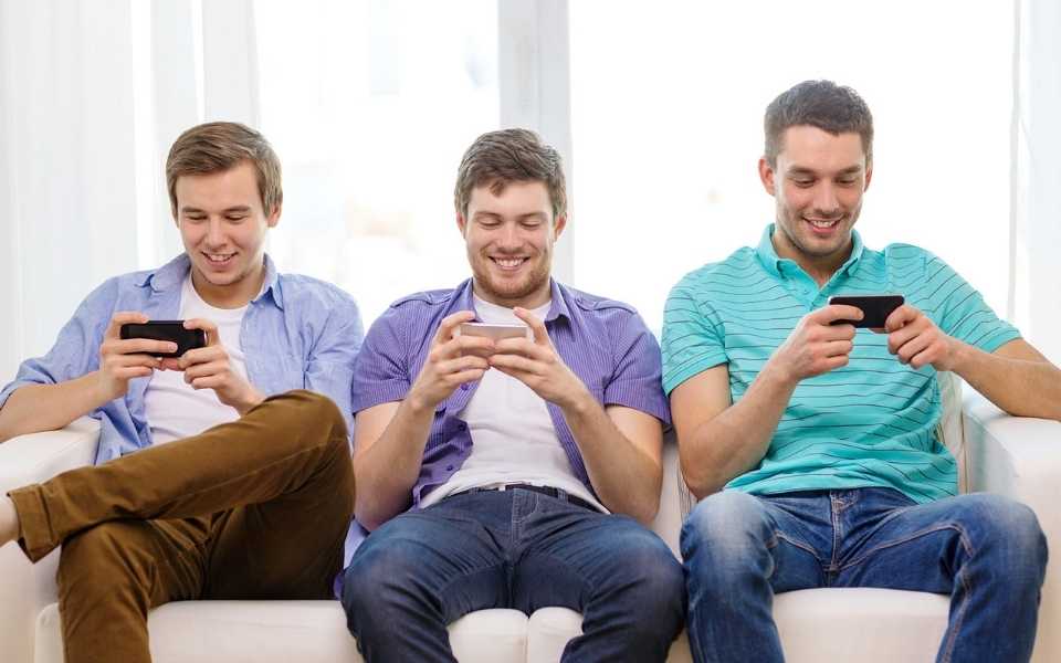 Three happy men playing video games with phones and wearing summer clothes. Concept of language translation and games localisation.