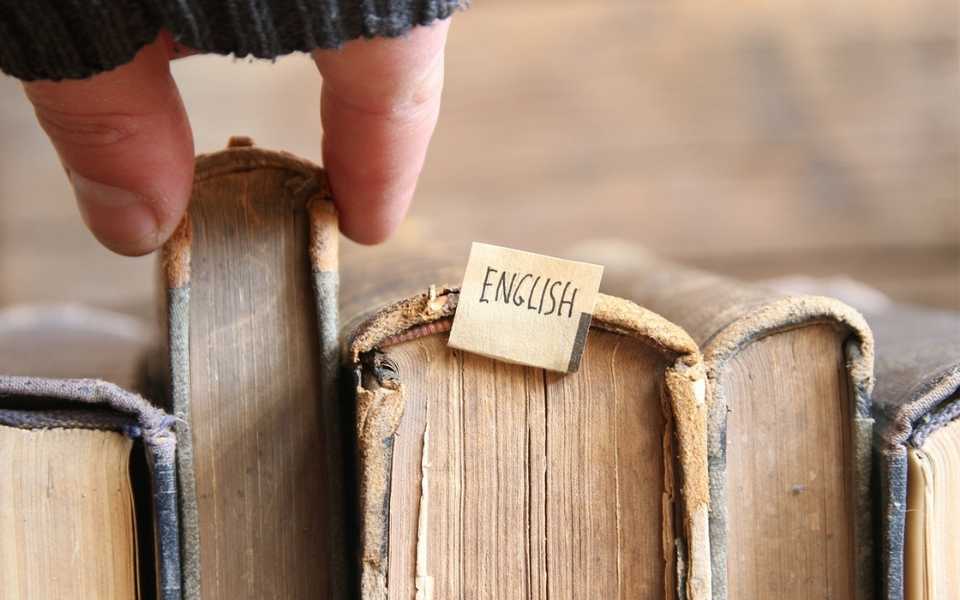 A group of old books, one labelled English, and someone choosing a book. Concept of translating to English.