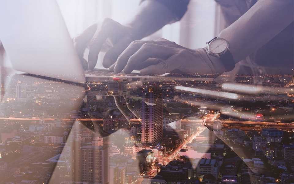 A young man's hand typing on a laptop over the city at night. Concept of technical translators.