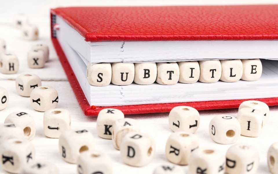 A red leather book and many lettered wooden cubes spread around it. Concept of subtitling and captioning services.