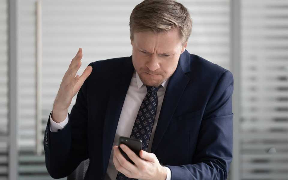 A businessman raises his hands and looks nervously at mobile. Concept of brand name translation.