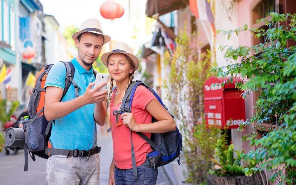 A couple carrying travel and camping backpacks, looking at the phone. Concept of tourists who must know Chinese words for summer festivals.