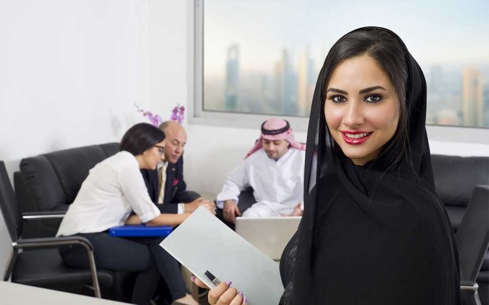 An Arab employee wears an abaya, behind her, employees are discussing work. Concept of translating to Arabic.