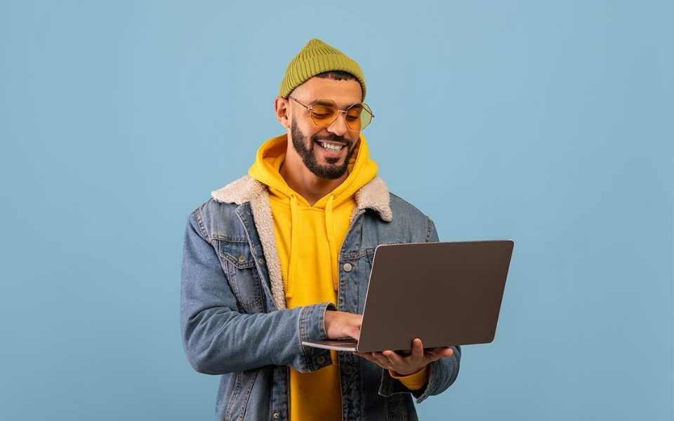 An Arabic man standing with a laptop in his hand and smiling. Concept of eCommerce website translation by professional translators for Arabic.