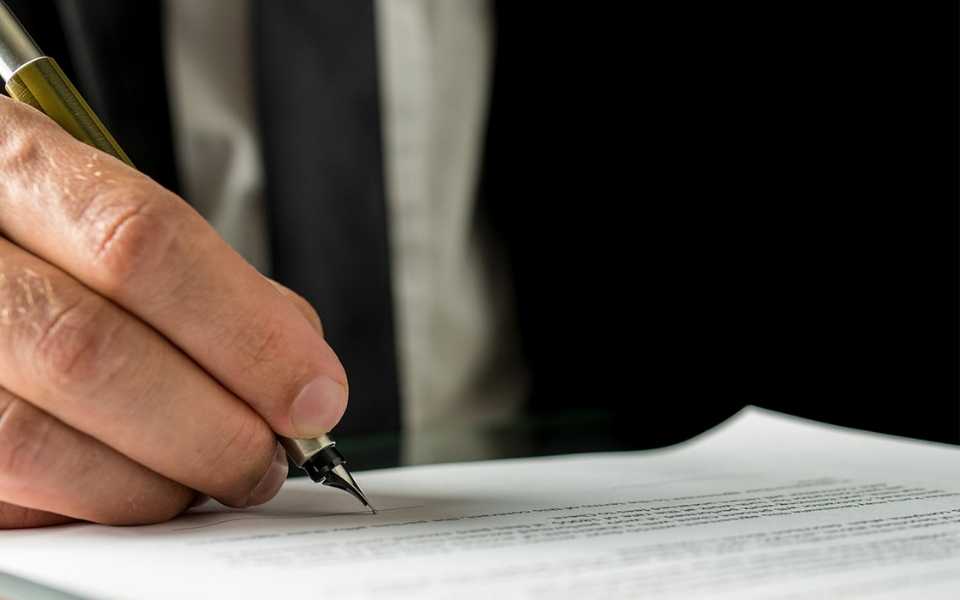 A businessman wearing a formal suit, signs papers in the company. Concept of certified translation services and UK translators.