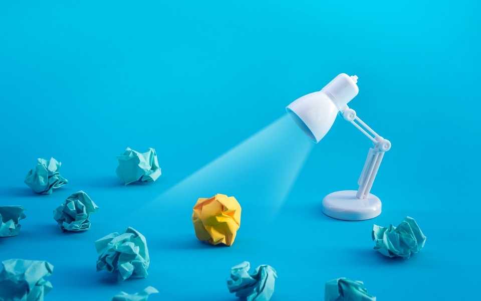 Blue crumpled paper balls, one yellow, with desk lamp shining on them. Concept of transcreation services.