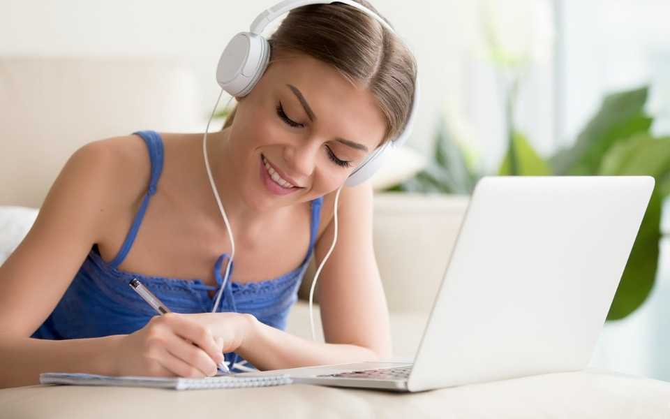 Girl with headphones writing on a notebook, with a laptop. Concept of learning languages.