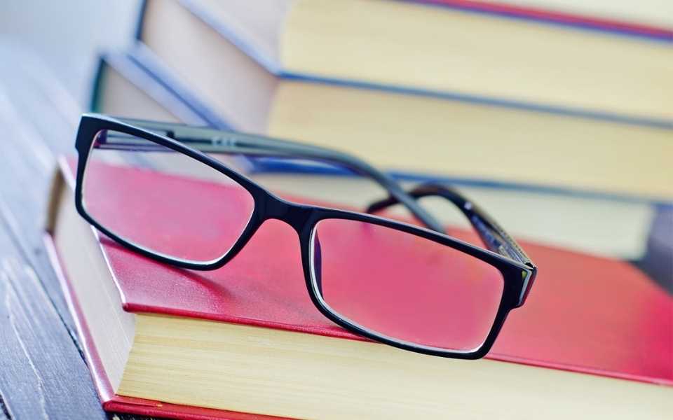 Medical glasses placed on a red book, next to several other books. Concept of editing and proofreading services and professional editors and proofreaders.