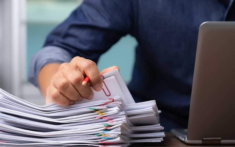 Man sitting on desk, holding a pencil, using a laptop and working on files. Concept of translating documents by a freelance translator or a translation company.