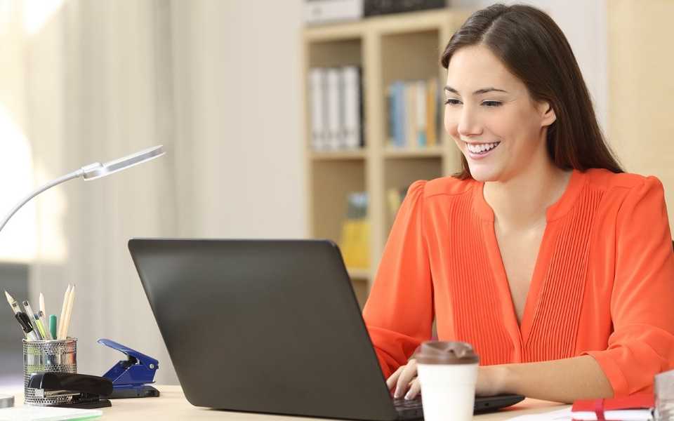 A woman smiling while working on a laptop in an office. Concept of social media translations.