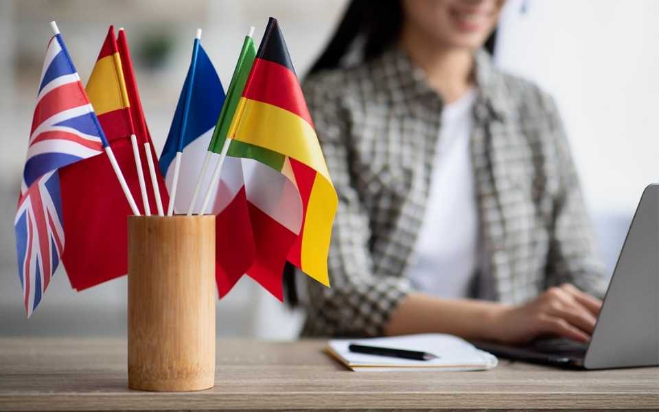 A cup with flags and a woman using a laptop. Concept of translated languages.