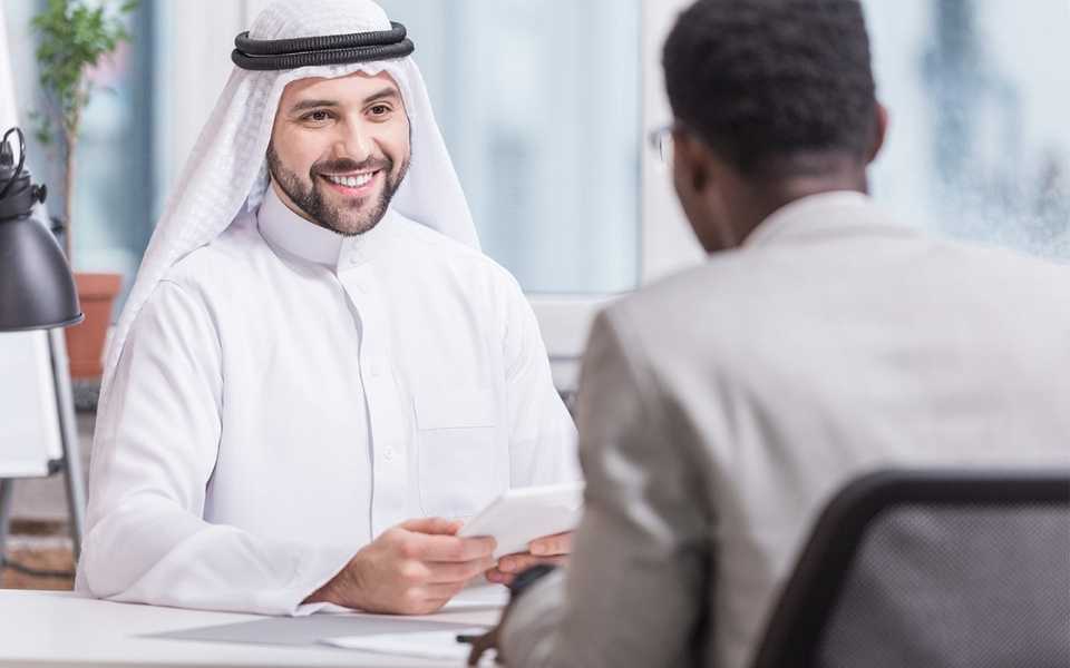 An Arabic man smiling at the man sitting in front of him. Concept of Arabic translation services.