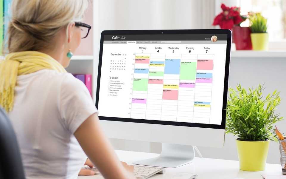 Professional woman sitting on desk and using calendar on computer. Concept of time management strategy.