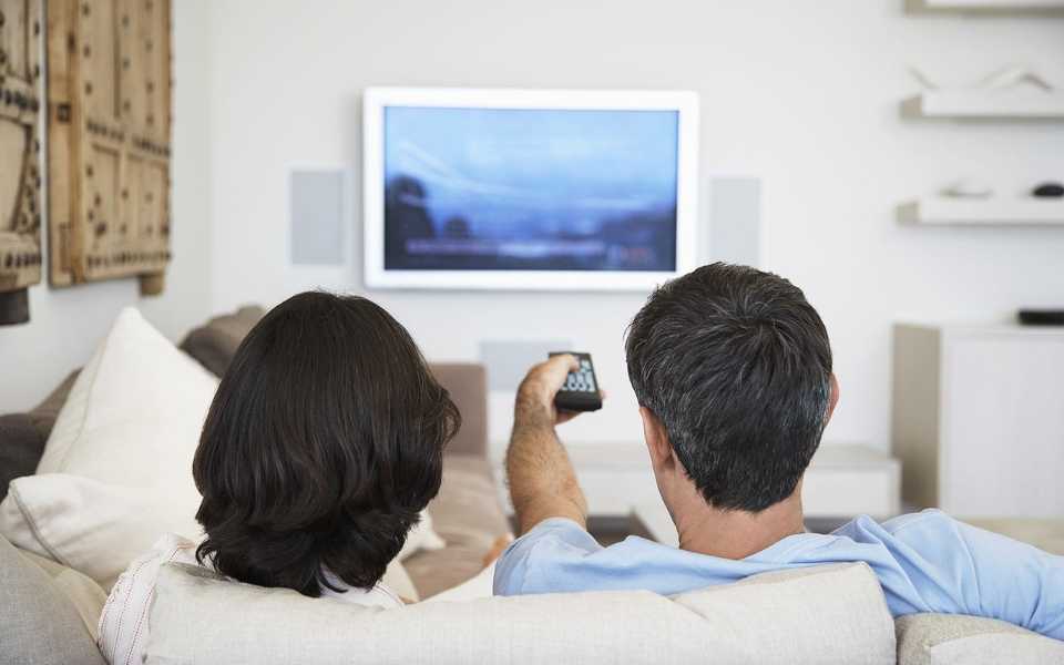 Couple watching TV, one of them holding the remote control. Concept of subtitling service.