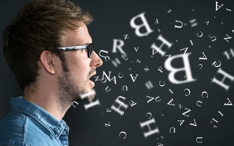 Young man wearing glasses and talking with English letters coming out of his mouth. Concept of language translation agency.