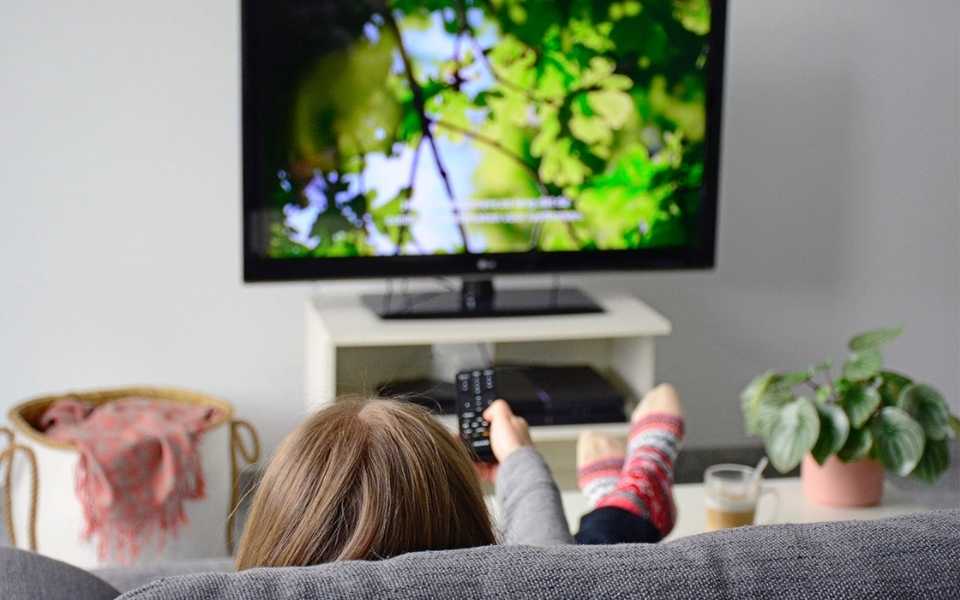 A girl sitting comfortably on the sofa at home and watching movies on TV. Concept of subtitling services for movies and else by professional subtitling companies.