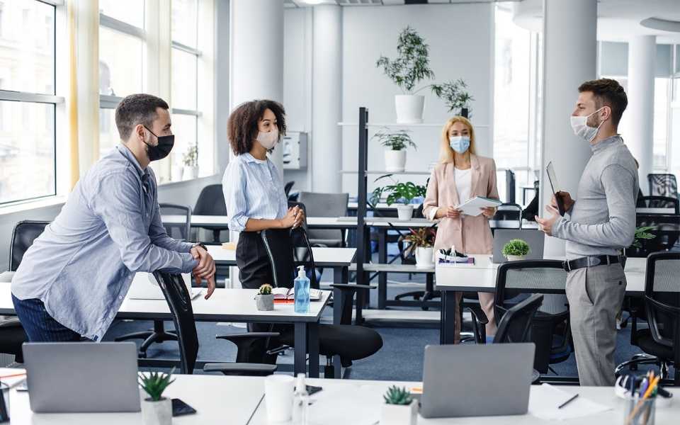 Two men and two women standing in office and wearing masks. 