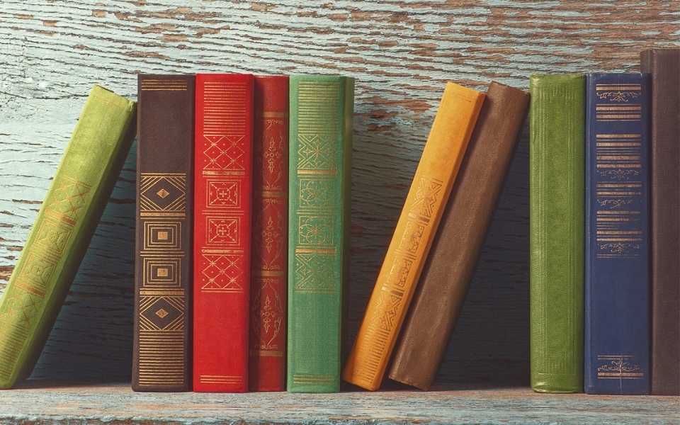 A group of old books with bold-coloured covers on a wooden shelf. Concept of translating books.