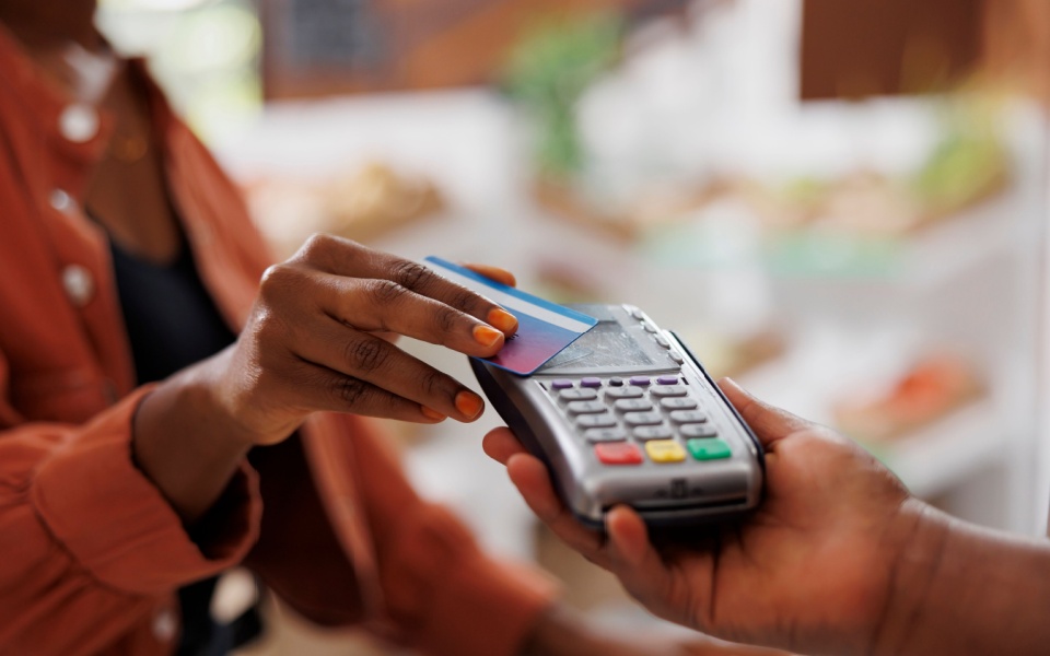 African man using credit card to make contactless payment at grocery store. Retail translation services. 