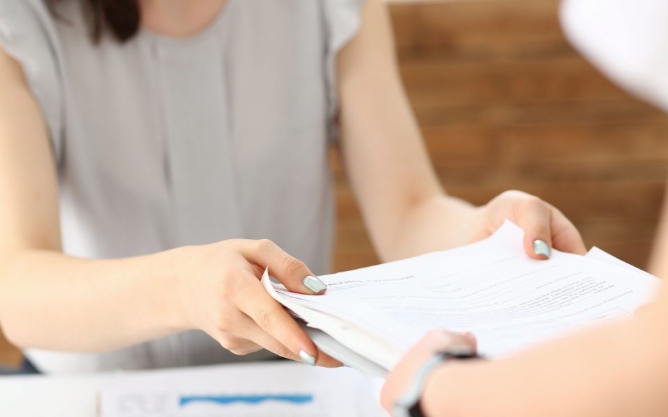Female employee handing in pile of documents for business translation to another busy employee. Translation services for businesses.