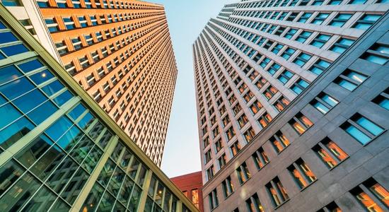 A low angle picture of two skyscrapers, one orange, the other gray. 