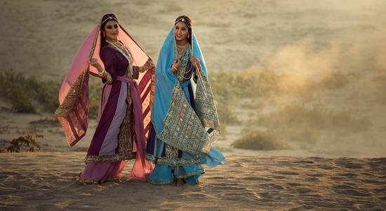 Two women in the desert in Farsi dresses, one purple, one blue. Concept of professional Farsi translators.