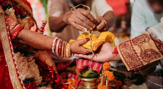 The hands of three Bengali women performing a ritual with yellow cloth.
