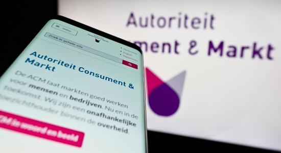 The website of Dutch regulator Autoriteit Consument en Markt viewed on mobile phone and a screen in the background.
