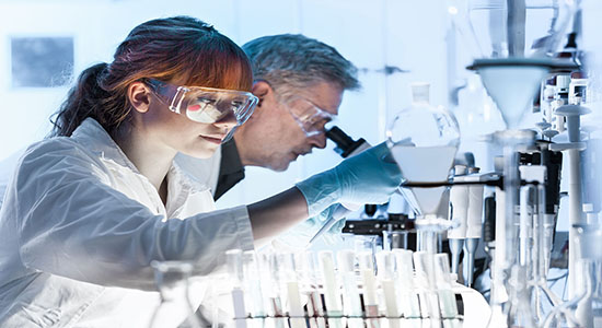 Male and female researchers using microscope in life science laboratory.