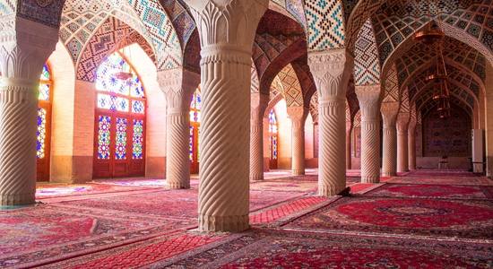 Interior of Nasir al-Mulk Mosque, with ornate archways and red prayer carpets. 