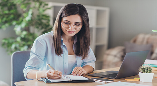 Young woman working and typing on laptop keyboard and taking notes.