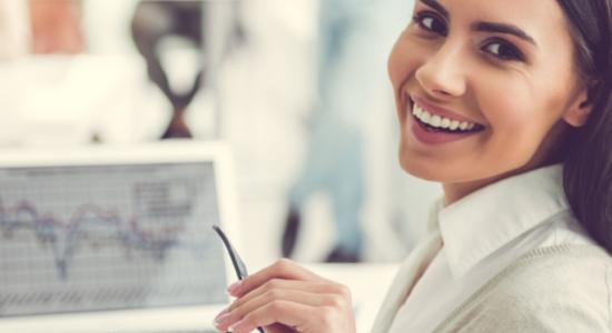A professional woman working on laptop while turning her back and smiling at camera. Concept of technical Spanish translation.