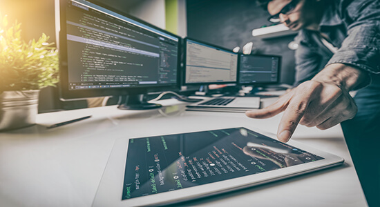 A developer working in office with tablet and computer screens.