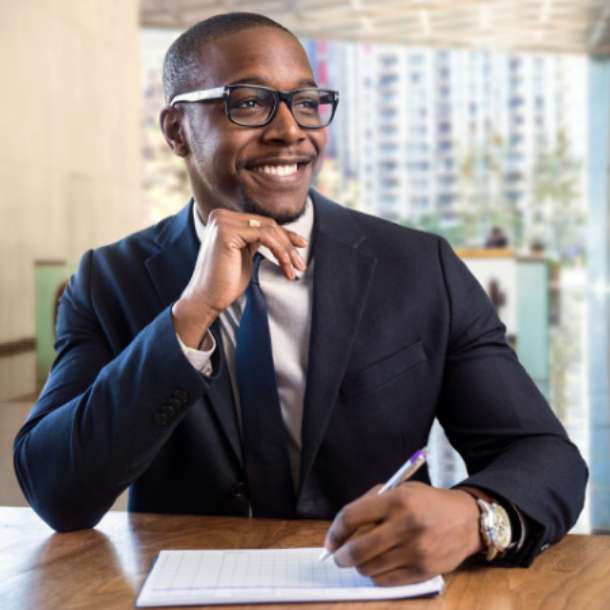 African man wearing suit and glasses smiling and signing paper. A concept of professional Albanian translator.