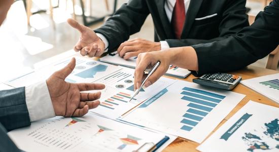 Three men discussing, working and pointing at financial documents on a table. 