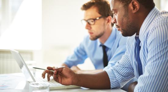 Two men work on computer. 