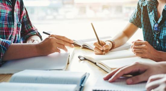 Three men working on table with pencils in hand. 