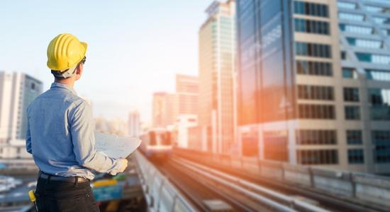 An engineer seen from behind looking at a skyscraper, clipboard in hand.