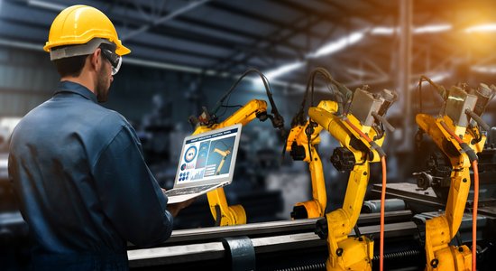 Engineer looking at laptop displaying smart industrial control panel of yellow machine. Concept of industrial and manufacturing technical translation services.