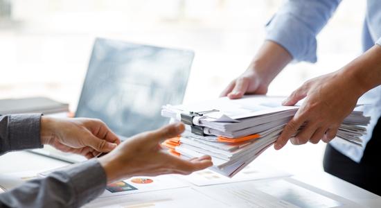 Professional man handing in stack of documents to another man. 