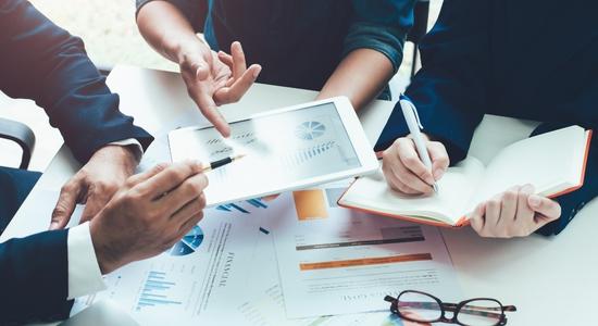 Two men and one woman working and pointing at tablet and financial documents. 