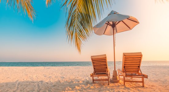 Two wooden lounge chairs on a beach at sunset. Concept of travel and tourism translation.