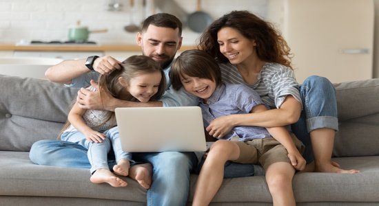 A family of four on a sofa smiling looking at a laptop.