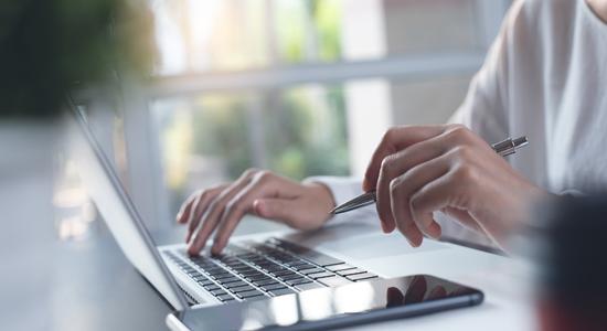 A person working on a laptop with a pen in one hand. Concept of e-learning localisation.