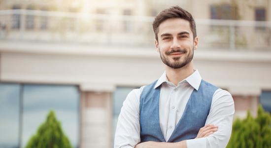 A man in dress shirt and waistcoat outside, smiling at camera.