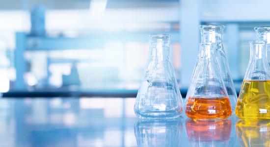 Close-up of Erlenmeyer flasks, some with chemicals, on a lab counter. Concept of biological translation services.