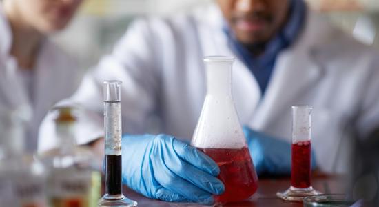 Scientist in lab gear working with chemicals in tubes and flasks. 
