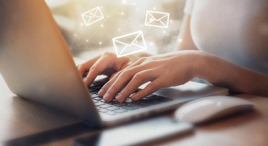 Two hands typing on a keyboard, email symbols hovering above. 